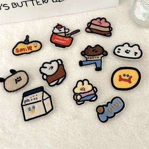 Detailed view of 11 assorted cute cartoon plush embroidery patches on white fabric