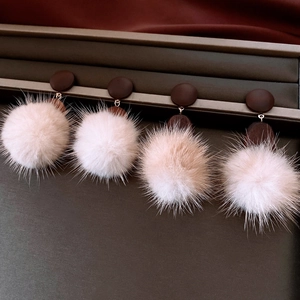 Detail of round fluffy pink pom-pom drop earrings with dark brown studs on a jewelry tray