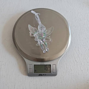 Clear acrylic cupid ornament with iridescent coating being weighed on a digital scale