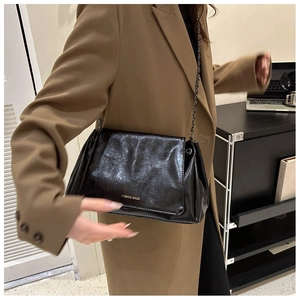 Detail view of the black leather shoulder bag with a fine gold metal chain strap on model