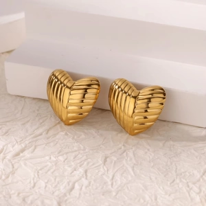 Macro shot of gold heart stud earrings with striped texture on a white tiered stand
