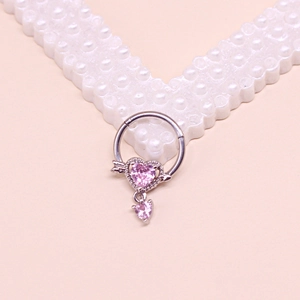 Detailed view of silver heart navel ring with pink gemstone and arrow on pink background