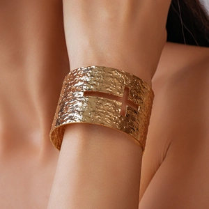 Detailed close-up of wide golden hammered metal cuff bracelet with cross cutout detail