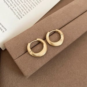 Detail of matte gold circular hoop earrings placed on a soft brown display stand