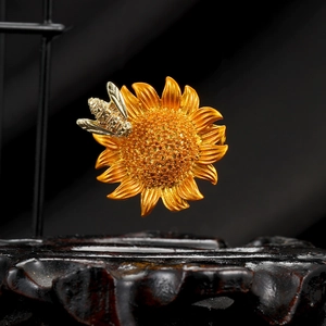 Elegant gold bee and sunflower brooch with detailed metallic texture on a dark display