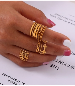 Detail of layered gold geometric rings set with cutout textures and leaf motifs on model hand
