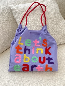 Close-up of purple nylon tote bag with colorful towel embroidered text and red handles