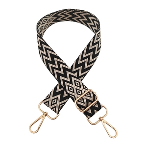 Detail of adjustable woven black and beige bag strap with gold metal hooks and buckle
