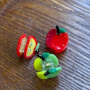 Detail of red and green acetate apple hair clips on a vintage brown wood background