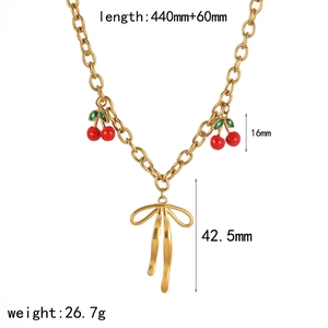 Gold cherry necklace with bow pendant, green leaves and red charms on white background