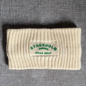Detail eines cremefarbenen Strickstirnbands mit Rippenmuster und grüner Stickerei