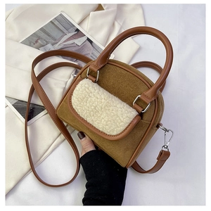 Detail of a brown suede handbag featuring white faux shearling trim and leather handles