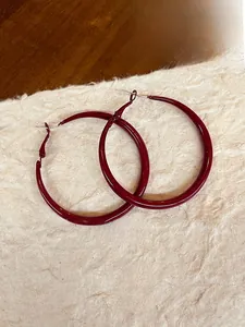 Detail of dark red enamel hoop earring on textured paper with an elegant French aesthetic