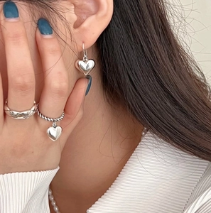 Close-up of 925 sterling silver heart earrings and textured rings on model