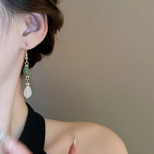 Detailed view of long water drop earrings with green beads and white pendant on model