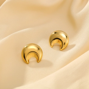 Polished gold crescent moon stud earrings in stainless steel on beige silk fabric