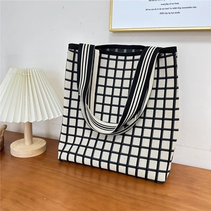 Macro detail of black and white checkered knit tote bag on wooden desk with lamp