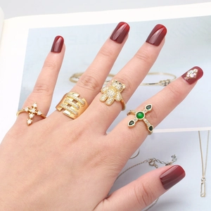 Golden rings set with bear motif, cross design, and green gemstone worn on model hand