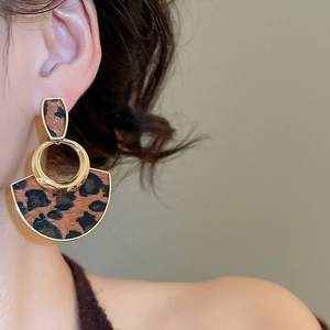Close-up of golden vintage leopard print round earrings worn by a model in soft light