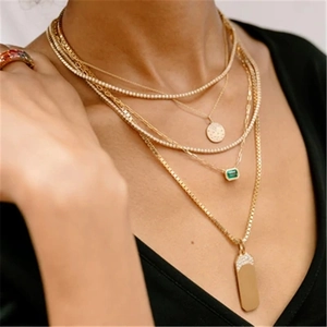 Close-up of layered gold necklaces with emerald pendant and rainbow gemstone ring