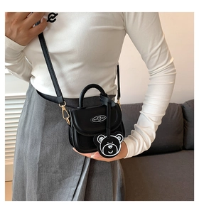 Detail of black mini crossbody bag with a cute bear charm and curved handle