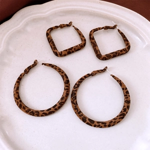 Macro view of leopard print flocked square and round hoop earrings on a ceramic dish