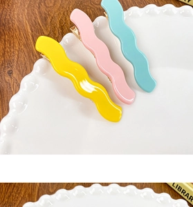 Close-up of three wavy acetate hair clips in yellow pink and light blue on a white plate