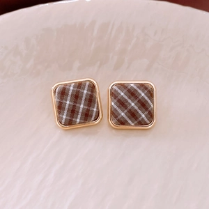 Détail d'une boucle d'oreille carrée avec bord doré et tissu à carreaux brun