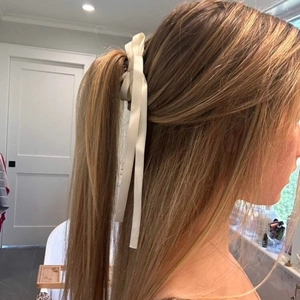 Detail view of a creamy white silk bow hair clip with long ribbons on a ponytail