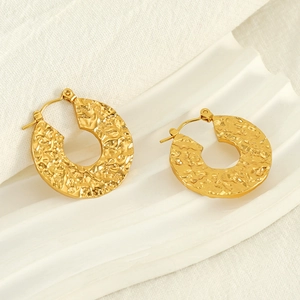 Macro detail of gold hammered texture hoop earrings on a minimalist display stand