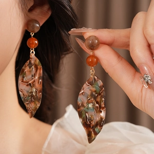 Detail of amber acetate leaf earrings with resin beads and gold-tone links on a model