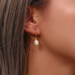 Close-up of elegant gold drop earrings with white cat eye stone worn by a model
