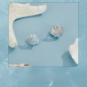 Detailed view of silver shell and starfish earrings with blue enamel on water ripple background