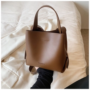 Close-up of brown leather bucket bag with top handle and embossed logo on white fabric