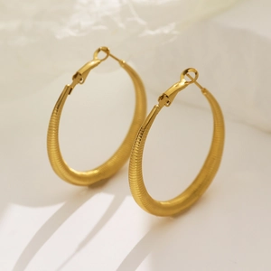 Macro detail of golden hoop earrings featuring a textured spiral finish and polished surface