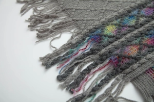 Detailed view of dark grey knit shawl featuring diamond patterns and long fringe tassels