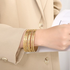 Dettaglio di sei bracciali rigidi dorati testurizzati indossati con un blazer beige raffinato
