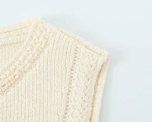 Gros plan sur la texture en maille et le bouton doré d'un gilet en tricot blanc cassé