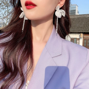 Gros plan de boucles d'oreilles fleurs en tissu blanc avec de longs glands de perles sur modèle