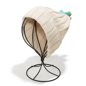 Detail of chunky cable-knit beanie in beige with unique teal top accent on stand
