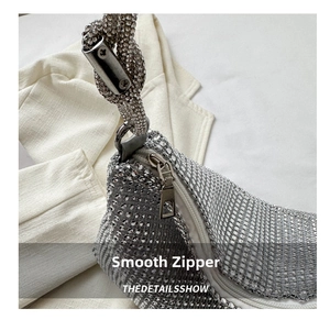 Detailed close-up of smooth metal zipper and knotted rhinestone strap on silver handbag