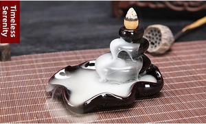 Macro view of a dark ceramic backflow incense burner with cascading white smoke on a bamboo mat