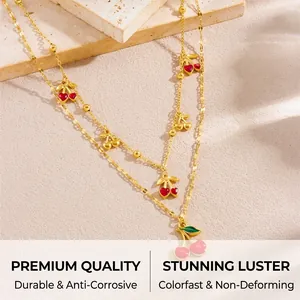 Macro detail of gold layered necklace with cherry pendants and red beads on stone base