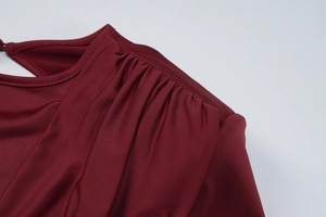 Dettaglio del vestito in maglia bordeaux con eleganti pieghe sulla spalla e scollatura