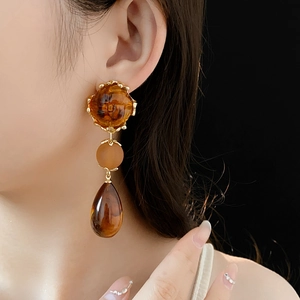 Detailed view of amber resin earrings with gold teardrop fringe on a model profile