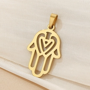 Macro shot of gold Hamsa hand pendant with heart cutout on white textured background