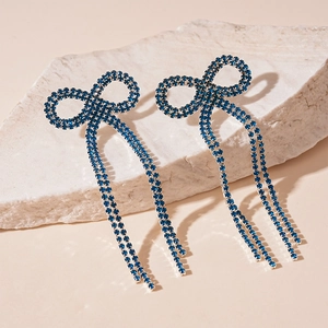 Détail de boucles d'oreilles nœuds en strass bleus avec pompons argentés sur roche