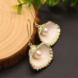Elegant gold shell earrings with white pearl and sparkling crystals on wooden base