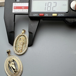 Detailed measurement of gold oval religious pendant showing 18.2mm width with cubic zirconia