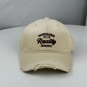Detailed view of distressed beige baseball cap featuring black letter embroidery design
